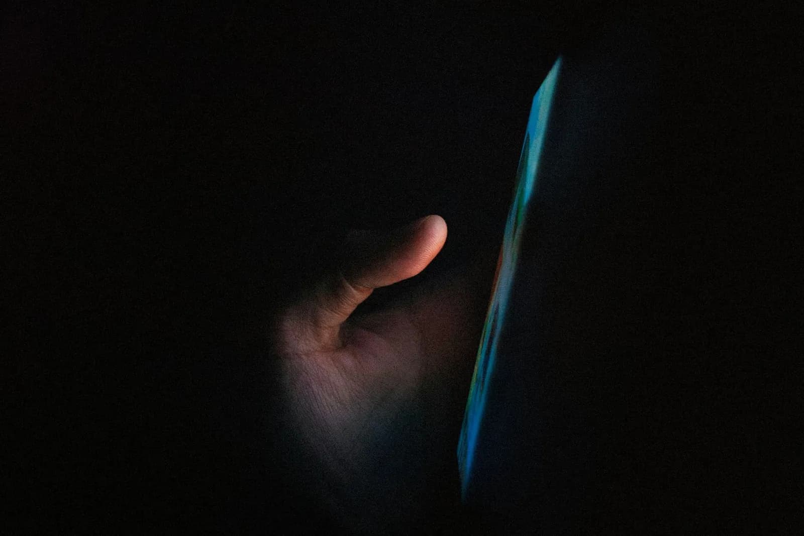 Hand hält ein Smartphone mit schwachem Leuchten im Dunkeln