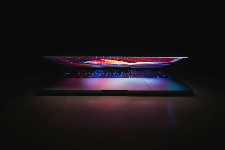 Halb geöffneter Laptop mit farbigem Leuchten im Dunkeln