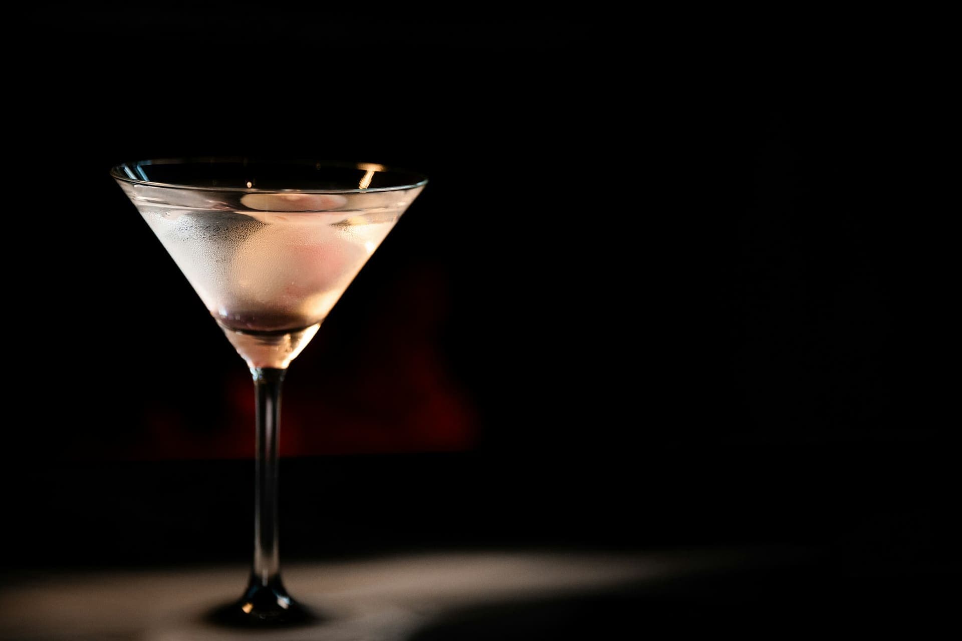 Cocktailglas im Lichtkegel vor schwarzem Hintergrund