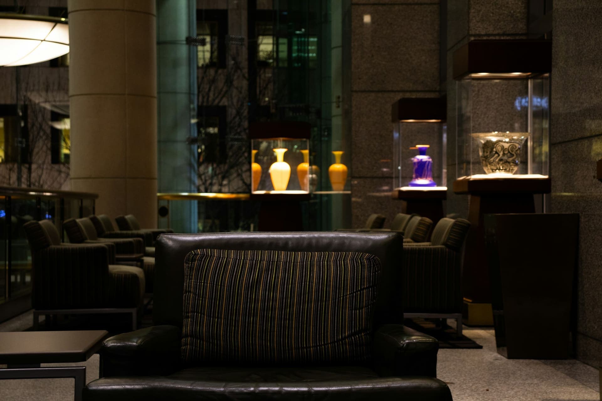 Dunkle Lounge mit Ledersesseln und beleuchteten Vitrinen