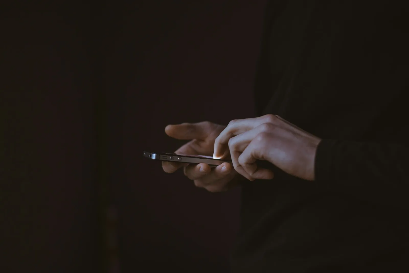 Hand hält ein Smartphone mit leuchtendem Bildschirm im Dunkeln