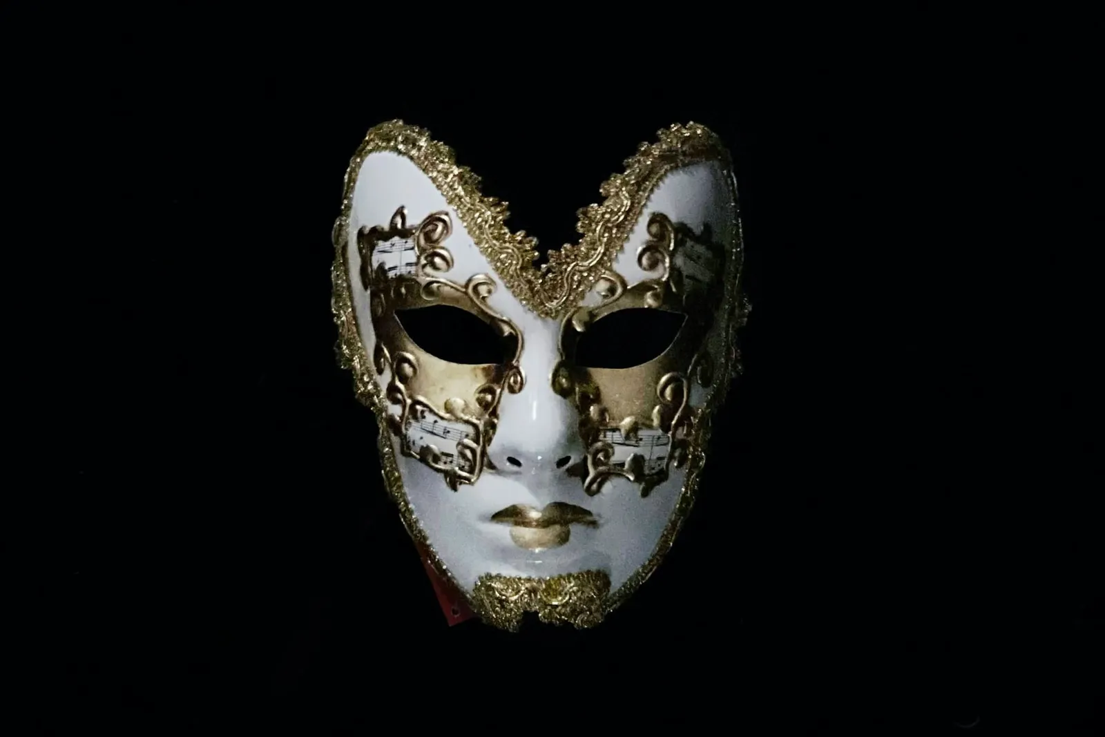 Weiße Maske mit goldenen Ornamenten vor schwarzem Hintergrund