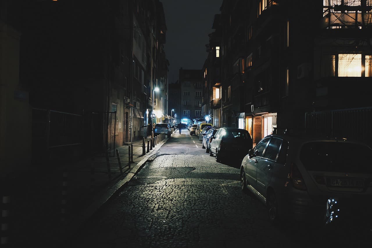Menschenleere nächtliche Gasse mit warmem Laternenlicht auf nassem Kopfsteinpflaster