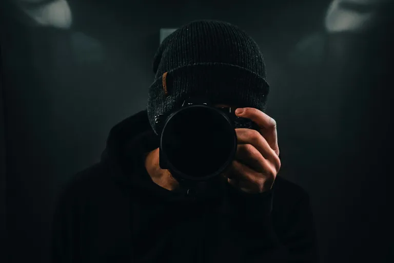 Fotograf mit Kamera vor dem Gesicht im Dunkeln