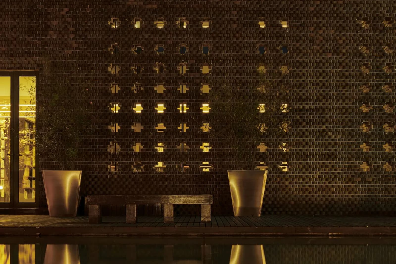 Warm beleuchtete Wand mit Lichtmuster, das sich in einem dunklen Becken spiegelt