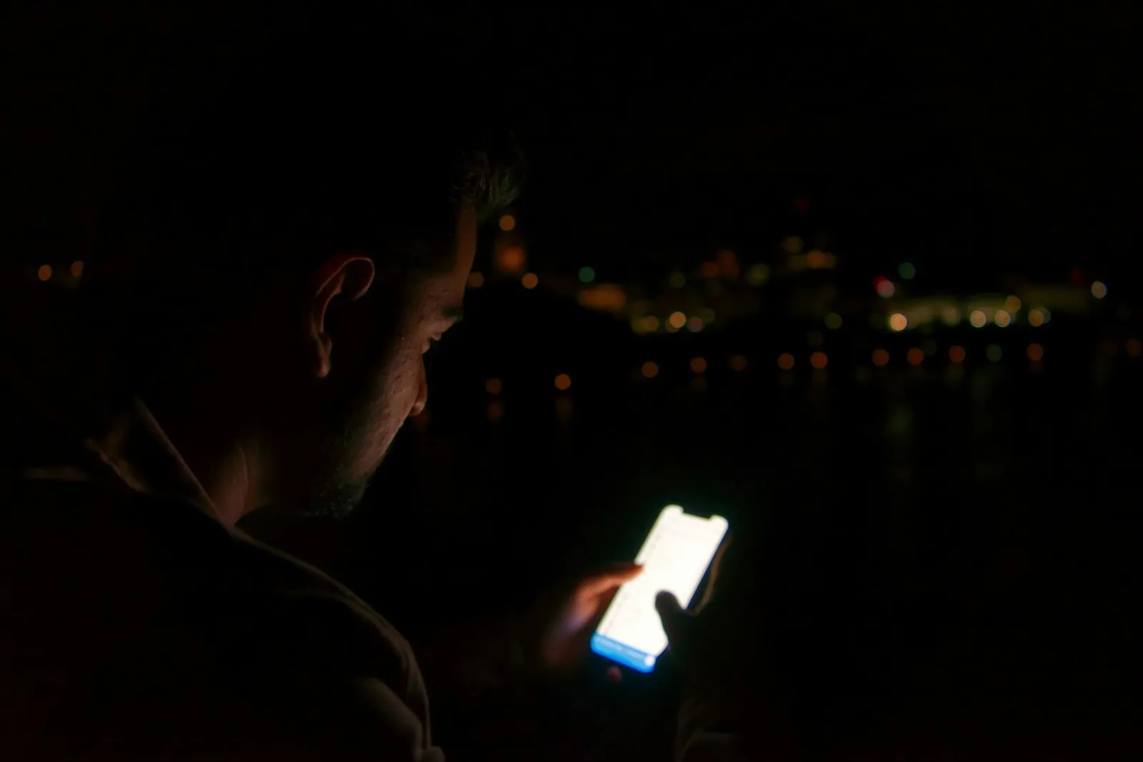 Mann blickt nachts auf sein leuchtendes Smartphone