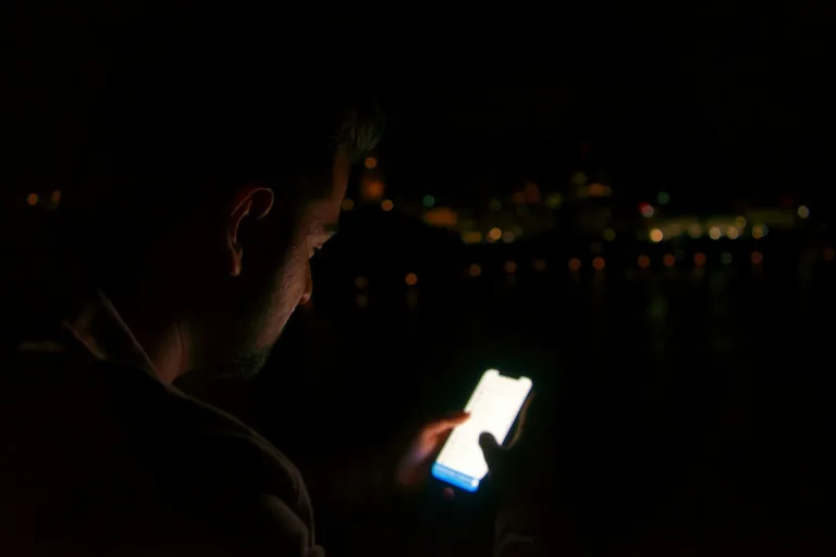 Mann blickt nachts auf sein leuchtendes Smartphone
