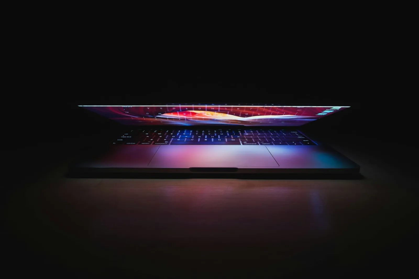 Halb geöffneter Laptop mit farbigem Leuchten im Dunkeln